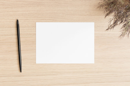 White invitation card mockup with a dry flower on the wooden table. Workspace concept. 5x7 ratio,...