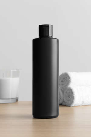 Black cosmetic lotion bottle mockup with a candle and towels on the wooden table.の写真素材