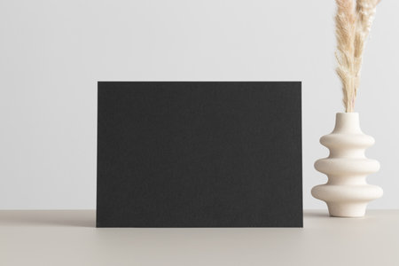 Black invitation card mockup with a  pampas decoration on the beige table. 5x7 ratio, similar to A6, A5.の写真素材