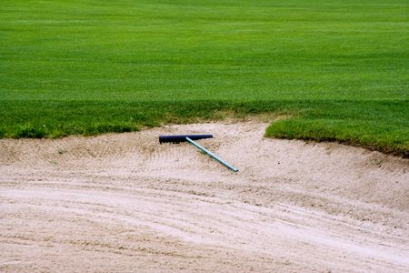 Sand trap on a golf course on the edge of the green with a rake laying in the sandの写真素材