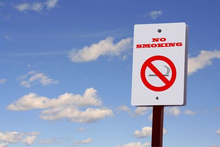 No smoking sign on a post against a blue sky with puffy white cloudsの写真素材