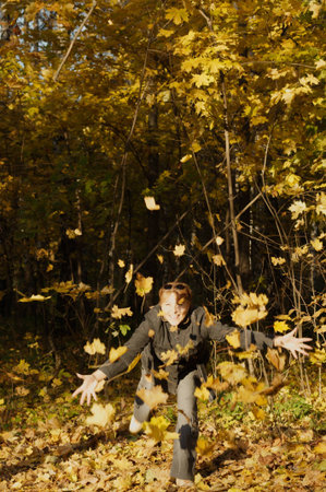 middle aged woman scatters leaves in autumn parkの写真素材