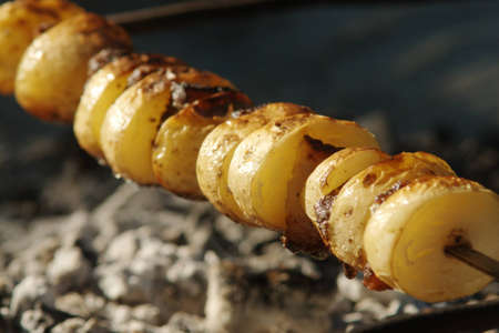 Baked potato with fat on skewer over coalsの写真素材