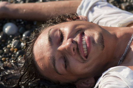 young smiling man lies on seacoastの写真素材