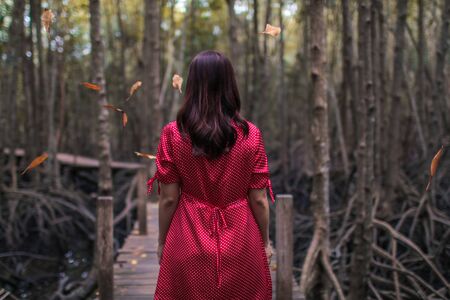 Beautiful young woman wearing elegant red dress walking on a forest path through the leaves of the trees in autumnの写真素材