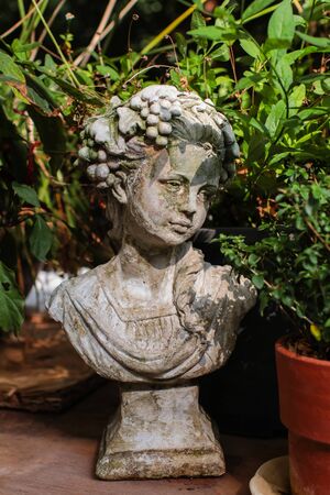 Closed up vintage style old stone statue garden sculpture with blurred green plants in backgroundの写真素材