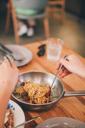 Spicy stir-fried spaghetti with fresh chilies, peppers, basil leaves and spaghetti,Spaghetti on a fork. Hand of woman rolling spaghetti and keeping on a fork for eat. Beautiful colorful and light bokeh at night in the background.の写真素材