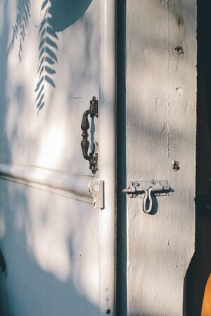 rusted latch lock white door. Front closeup shot of an old plank door of a barn locked with a pad-lock showing old color texture, grains and rust on the latchの写真素材