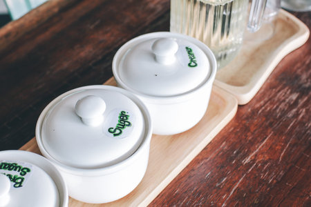 Ingredients sugar and cream white ceramic cup for coffee coffee with cream and tea spoon on saucer, milk jug, sugar cubes, package of sugar and creamerの写真素材
