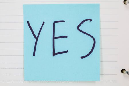 Close up black handwritten inscription yes word on blue square stickers It`s on a notebook School education objects isolated no people business successの写真素材