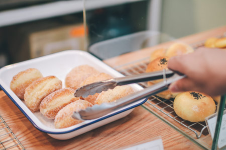 Closeup of woman holding clamp picking sugar-glazed doughnuts a bakery store.taking fresly baked bun...