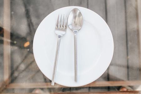 Place setting of a dining set of an empty plate with spoon, fork and knife over a rustic old wooden...