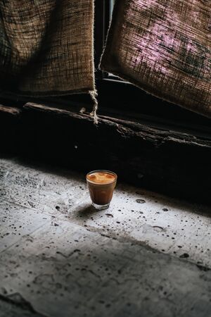 A cup of coffee on concrete floor near window vintage tone.Morning coffee cup.Hot drink glass helps to warm the body.With bright morning window light streaming through.の写真素材
