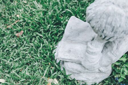 Backyard Statue Decorations on a sunny day the boy statue is sitting reading a book.Close up white stone boy angel statue in cute gesture with blurred green plants background in botanical garden, vintage styleの写真素材