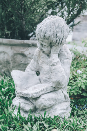 Backyard Statue Decorations on a sunny day the boy statue is sitting reading a book.Close up white...