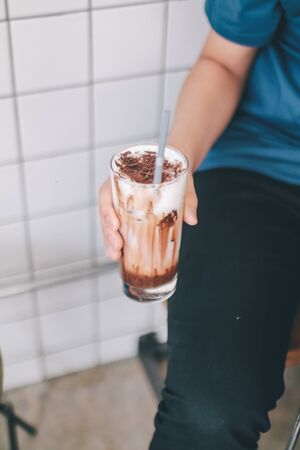 close-up hand holding the glass iced chocolate latte fresh milk mixed with cocoa sauce and milk foam on top making marble texture.の写真素材