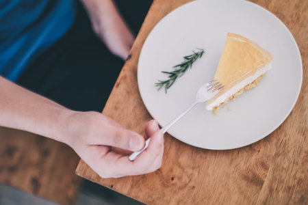 Man wear blue t-shirt sitting in coffee shop eating lemon cheesecake in white plate with folk.Tasty...