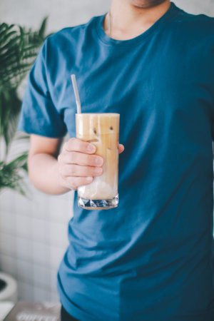 Man wear blue t-shirt holding ice coffee latte sit on chair at cafe.People having a break sitting in...
