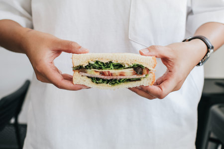Hand holding fresh delicious homemade sandwich with ham, cheese, bacon, tomatoes, lettuce, cucumbers...