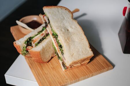 Close-up homemade ham,cheese,bacon, tomatoes, lettuce, cucumbers and onions with tomato sauce or ketchup on wooden cutting board.American unhealthy calories cuisine cooked by a man from a bun.の写真素材