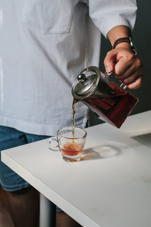 Close up man pouring hot tea from teapot  into small glass