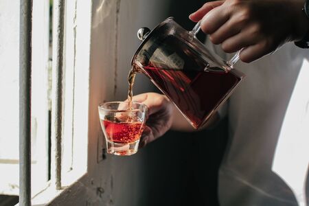 Close up man pouring hot tea from teapot  into small glass near window.の写真素材