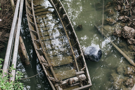 Wreck of a brown boat abandoned in the river.Vintage wooden boat sinking with leaves and water inside.damaged and left to rot rowing boat with stacked chopped wood on the background in countryside.の写真素材