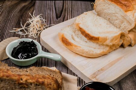 Close up fresh homemade loafs bread and sliced bread on cutting board with jam strawberry on woodenの写真素材