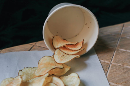 Fresh Crispy potato chips on a wooden background, top view. Salty crisps scattered on a table for a...