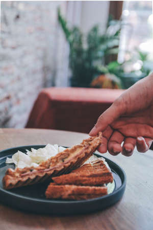 Hand pick up a piece of healthy Sandwich toast with ham, cheese and potato chip on black plate at breakfast time.の写真素材