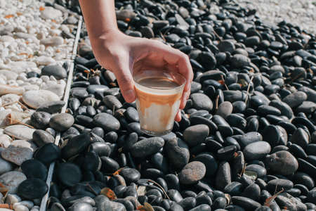 Hand pick up a glass of dirty coffee on black and white rock in garden floor. Background and texture of white and black pebbles stone. Take a break from work.の写真素材