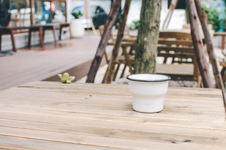 Close up of metal cup on old wooden table. Mockup of white enamel cup. Lifestyle relax. Top view,...