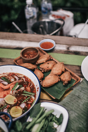 Fried Chicken Wings with Thai spicy sauce in white dish on wooden table top. Thai street food...