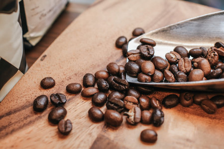 Dark roasted coffee beans in metal scoop on wooden background with copy space.