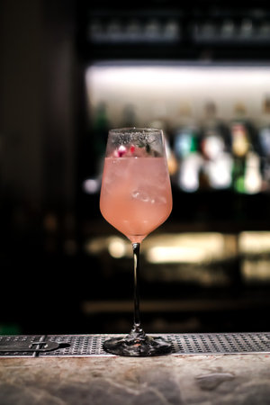 A gourmet mixed drink cocktail of sweet pink lemonade vodka and gin martini, garnished in the bar with bottles in the dark backgroundの写真素材