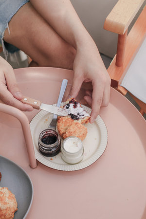 Hand spreads English Scones with Cream Cheese and Strawberry Jam, A scone is a single-serving quick...