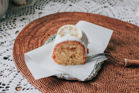 Slice of a lemon cake with sugar frosting in a ceramic plate, fork, lemons on rustic wooden...