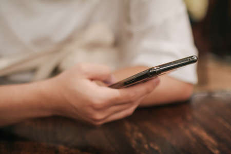 Close-up image of male hands using smartphone searching or social networks concept, hipster man typing an sms message to his friends on vintage wood table in cafeの写真素材