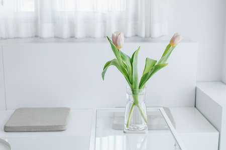 Pink tulips in a vase. Bouquet of flowers in the morning sun beams. Cozy home design and minimalism. Modern interior of living room or bedroom, vertical, close up, free spaceの写真素材