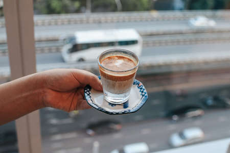 Man holding coffee cup in apartments with city view downtown background at the morning. Enjoy, lifestyle.の写真素材