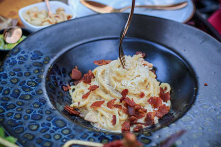 Delicious carbonara pasta with fried bacon, pancetta, egg, hard parmesan cheese and cream sauce. Traditional italian cuisine. Restaurant food concept.の写真素材