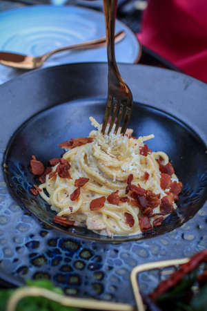 Delicious carbonara pasta with fried bacon, pancetta, egg, hard parmesan cheese and cream sauce. Traditional italian cuisine. Restaurant food concept.の写真素材