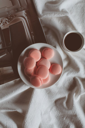 Pink macaron cookies with cup of coffee and rose flowers on white background. Spring still life scene. Vintage pastel styled photo. Copy space for you text. Toned image.の写真素材