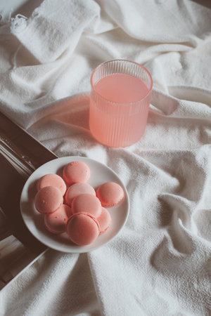 Pink macaron cookies with cup of coffee and rose flowers on white background. Spring still life...