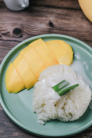Delicious mango sticky rice serve with coconut milk on wooden table. Popular traditional dessert of...