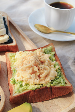 Breakfast with scrambled eggs, bread toasts, avocado and cup of coffee in morning light picnic...