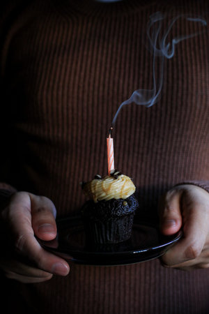 Chocolate Birthday cupcake with a single candle light on dark background.の写真素材