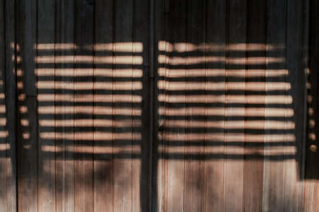 Shadows and sunlight on a brown wooden wall. Beams of sunlight through old window wooden blinds.の写真素材