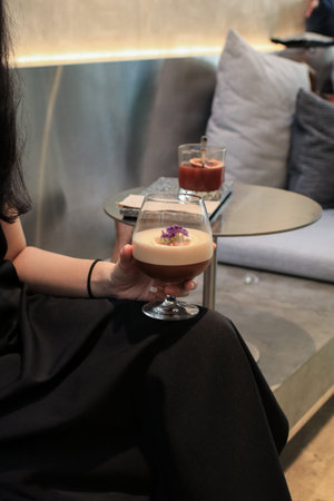 Woman hand holding Espresso mocktail in wine glass based on coffee and juice on wood background....