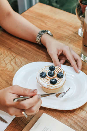 Hand pick up Lemon meringue and blueberry tart in white plate on wooden table. Pie Dessert. Horizontal Copy spaceの写真素材